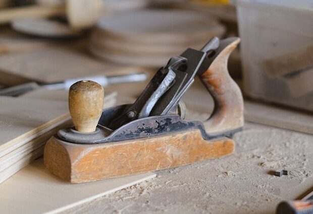 Hand plane for shaping wood placed on wooden table with instruments in joinery with various special equipment on blurred background