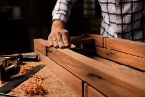 A close-up of a woodworker smoothing a wooden frame by hand in a woodworking shop.